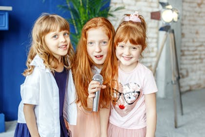Three girls with red hair smile and sing into a karaoke microphone