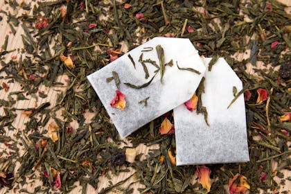 Tea bags lying in scattered loose leaf green tea and petals