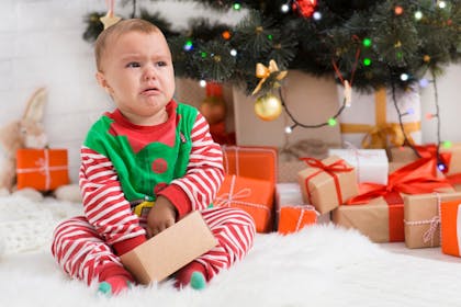 An angry baby dressed as an elf under a Christmas tree