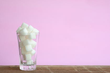 Glass of sugar cubes against pink background