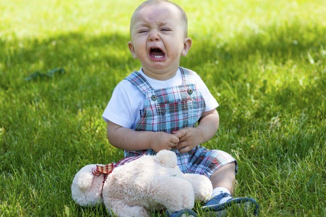 child and teddy bear sitting on grass