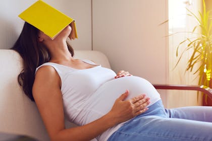 A tired and pregnant mum-to-be sat down with a book on her face