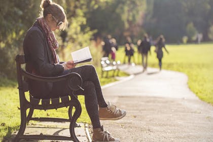 woman sitting on park bench reading book