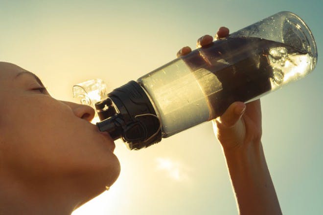 woman drinking water from a bottle with sun light behind her