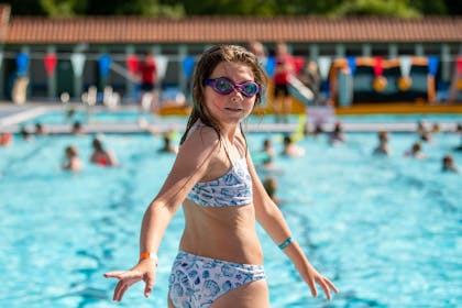 A girl in goggles and a bikini turns to smile before jumping into Lido Ponty