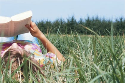 girl lying in field reading a book