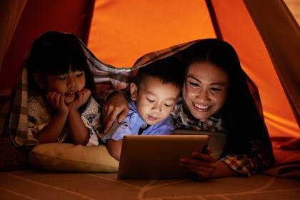 Mum and toddler boy and girl watch a film in a blanket fort
