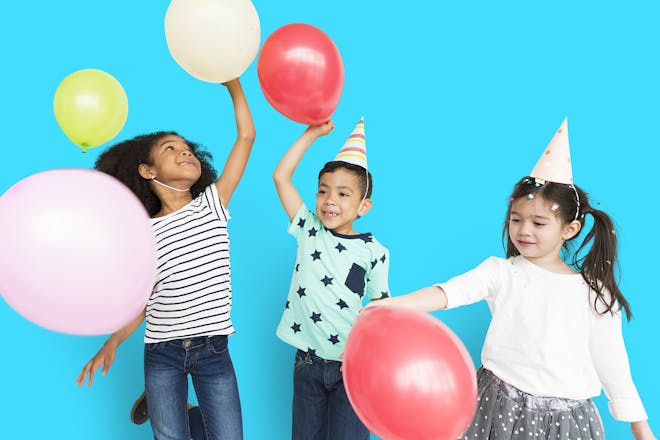 Three young children playing with balloons and wearing party hats