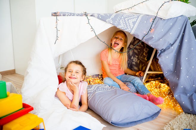 Two girls in a den made of pillows and sheets