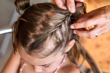 A little girl getting her hair braided by an adult