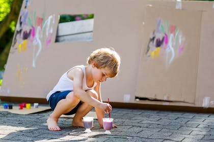 Kid outside painting house made from cardboard