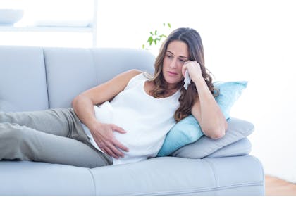Pregnant woman lying on sofa looking upset
