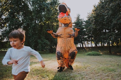 Man dressed as dinosaur chasing young boy