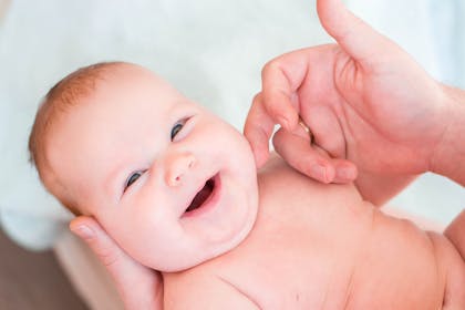 baby having cheek stroked by parent and smiling