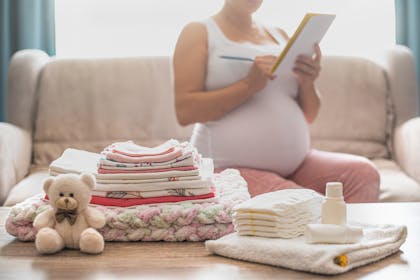 pregnant woman writing a list next to a pile of baby clothes