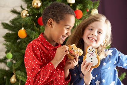 kids eating cookies in front of christmas tree