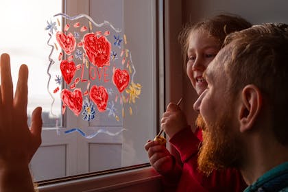 Dad and little girl paint love hearts on window