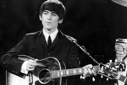 Black and white picture of George Harrison on stage with Beatles in 1960s