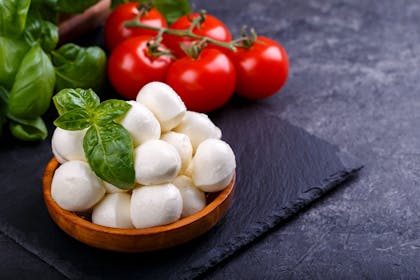 Mozzarella balls in a bowl next to basil and tomatoes