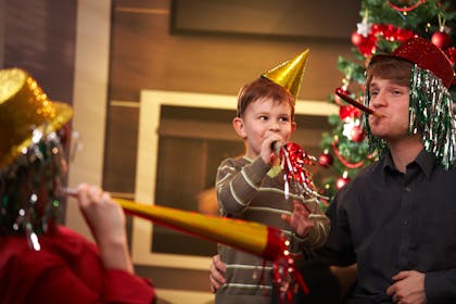 Family wearing shiny party hats and blowing party noise makers with Christmas tree in background