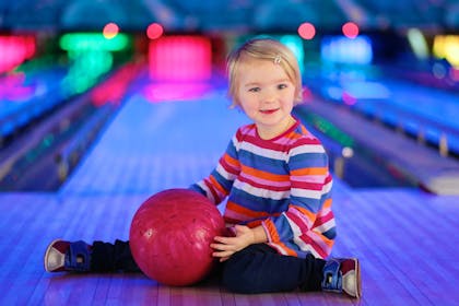 Toddler holding bowling ball at bowling alley