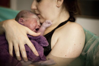 woman holding newborn in birthing pool at home