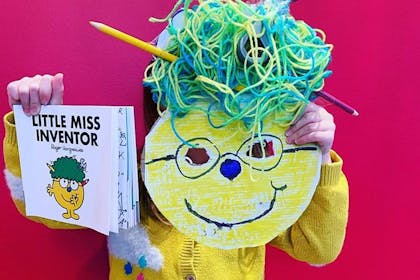 Kid dressed in Little Miss Inventor costume with book, cardboard face, woolly hair and a yellow cardigan