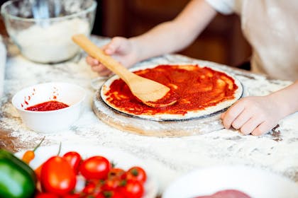Child putting tomato sauce on pizza base