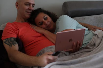Couple in bed watching something on a tablet.