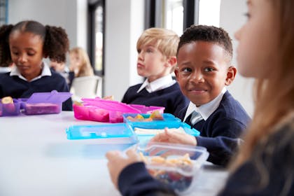 Primary school children at a table with lunch boxes