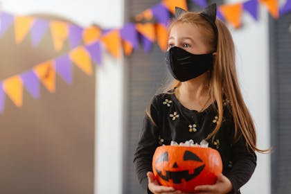 Girl dressed in Halloween costume with a mask on holding a pumpkin 