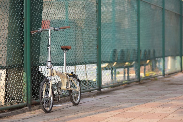 Un vélo pliant posé contre le grillage d'un cour de tennis