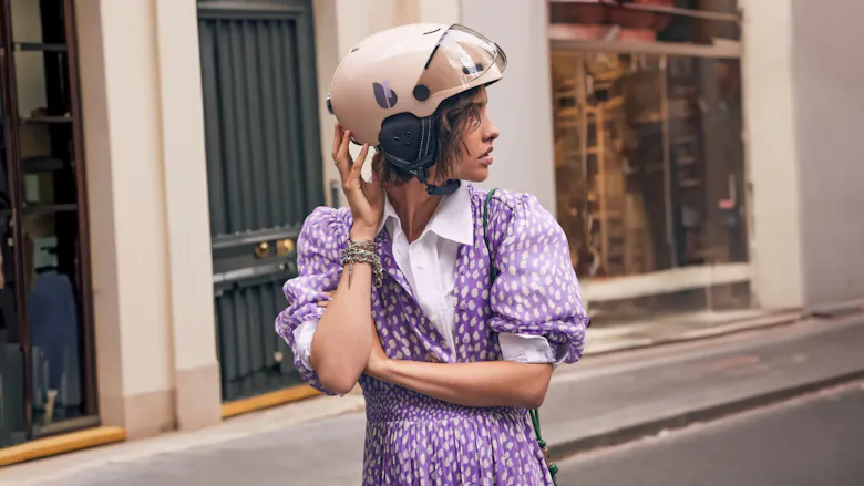 Une femme en robe violette portant un casque vélo beige de la marque Cosmo Connected