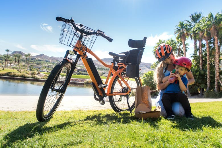 Une mère et son fils assis dans l'herbe à côté d'un vélo électrique reconditionné équipé d'une porte-bébé et d'un panier