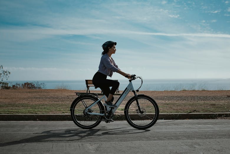 Une femme avec un casque vélo qui fait du vélo électrique en bord de mer