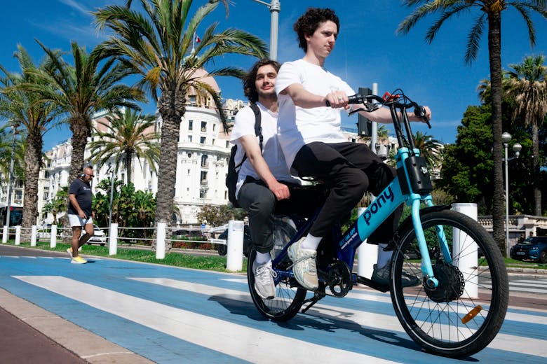 Deux jeunes hommes sur un vélo deux places, à Nice devant le Negresco