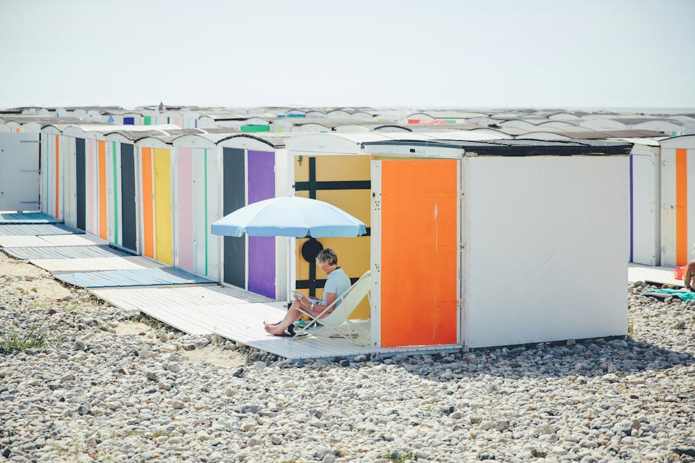 Une personne assise sur une chaise grise devant des cabine sur une plage au Havre