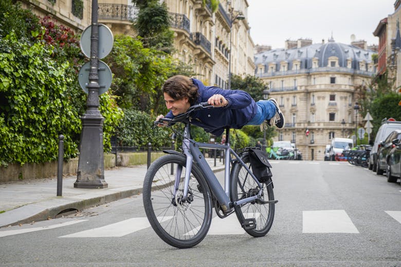 Un jeune homme qui fait la planche sur un vélo électrique dans une rue de Paris