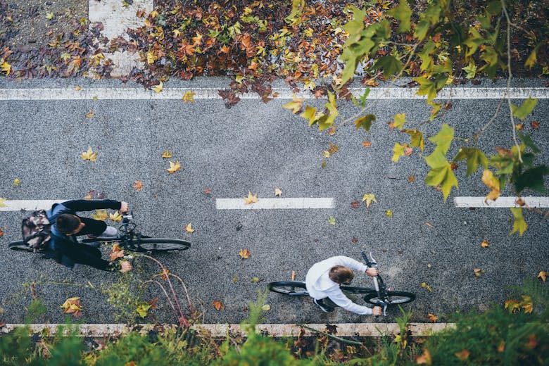 Deux cyclistes vus en plongée, sur une piste cyclable sécurisée bordée d'arbres