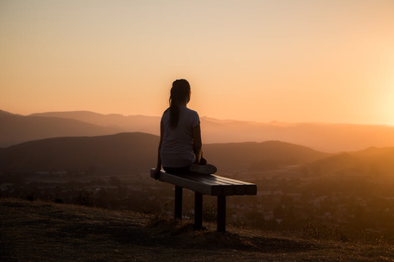 Une femme se relaxant sur un banc devant un coucher de soleil