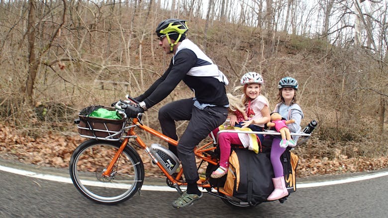 Un père de famille qui transporte ses deux filles sur une remorque vélo