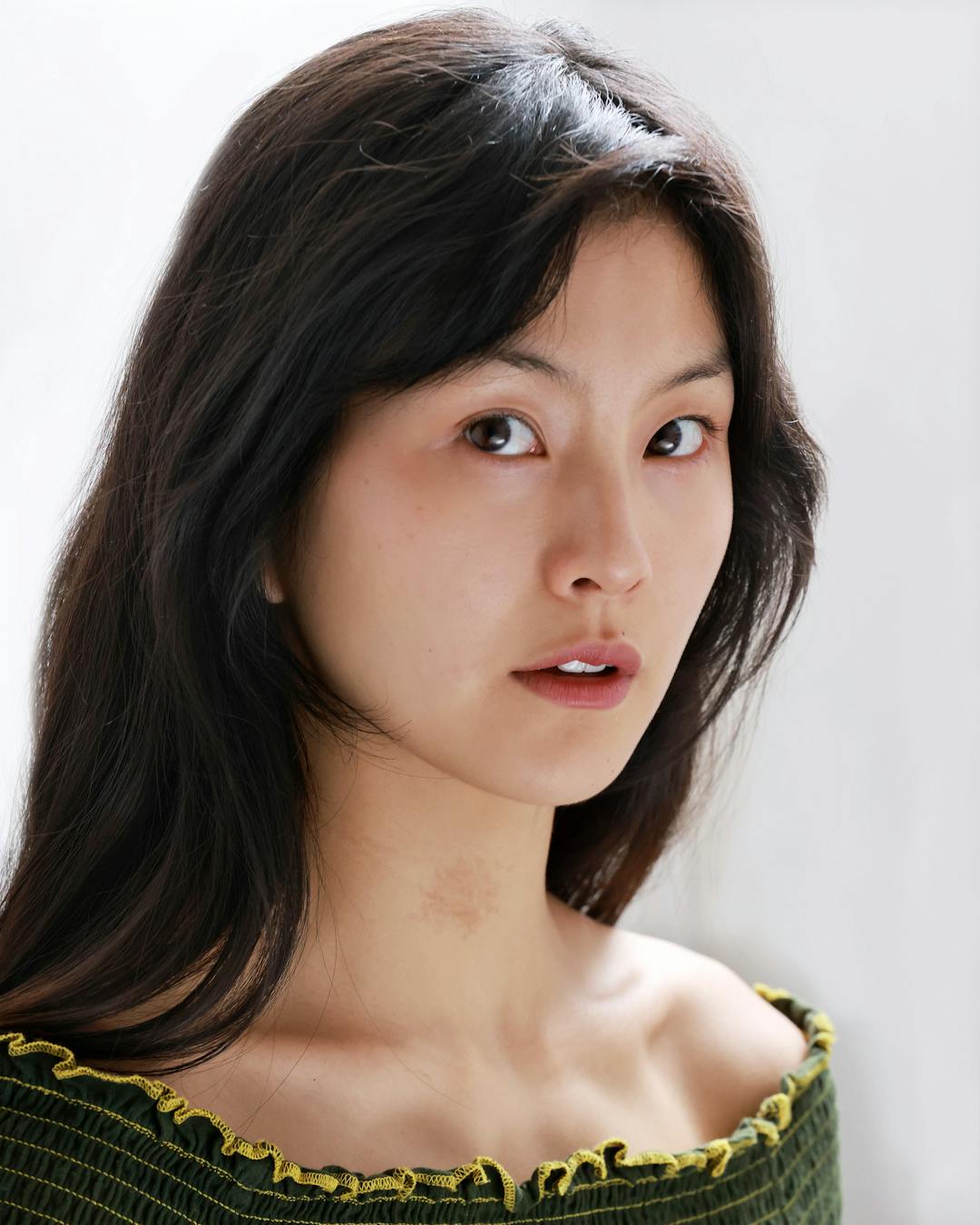 Young East Asian woman with dark brown hair falling past her shoulders and a green off the shoulder top.