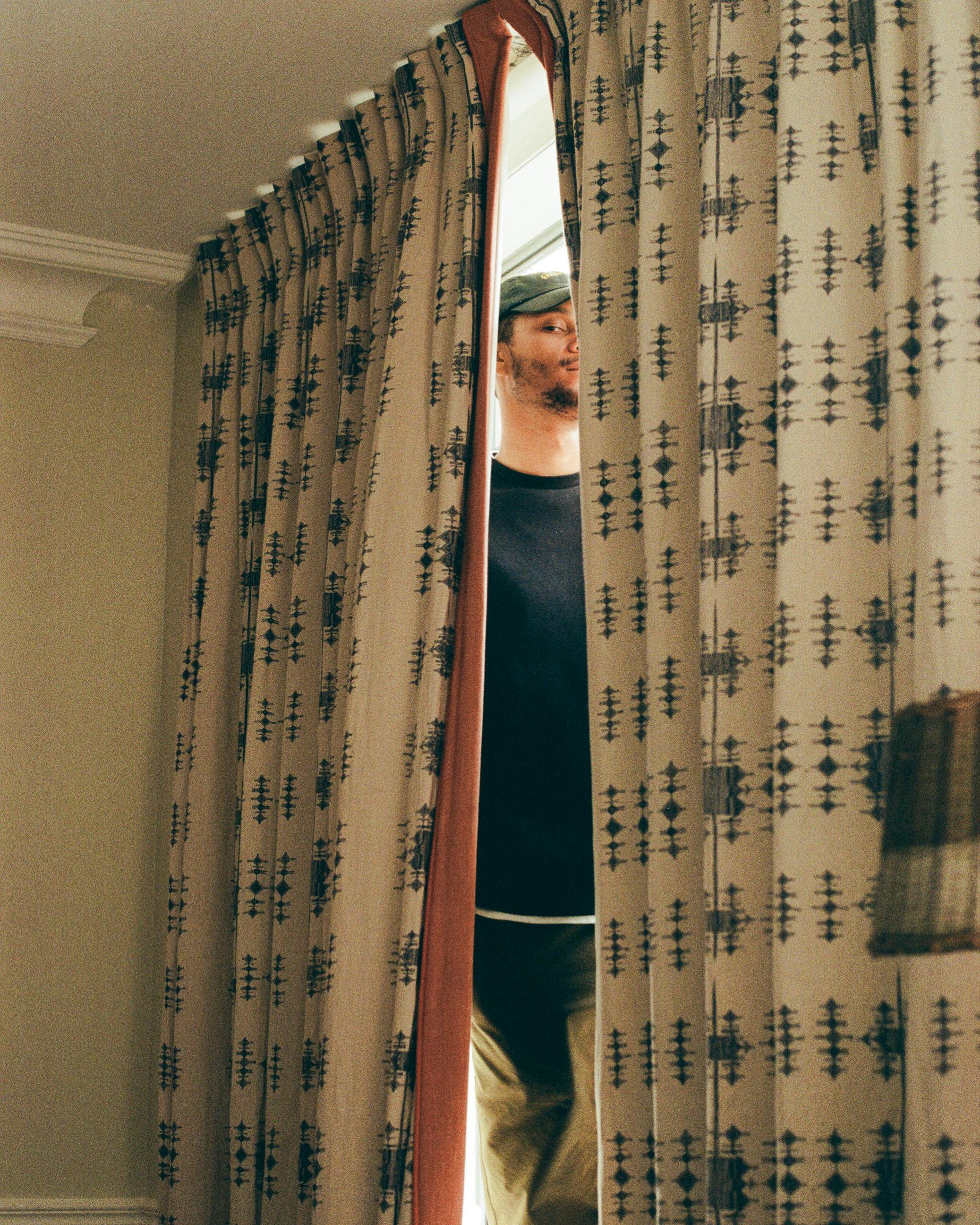 Jordan Spence looking through a curtain.