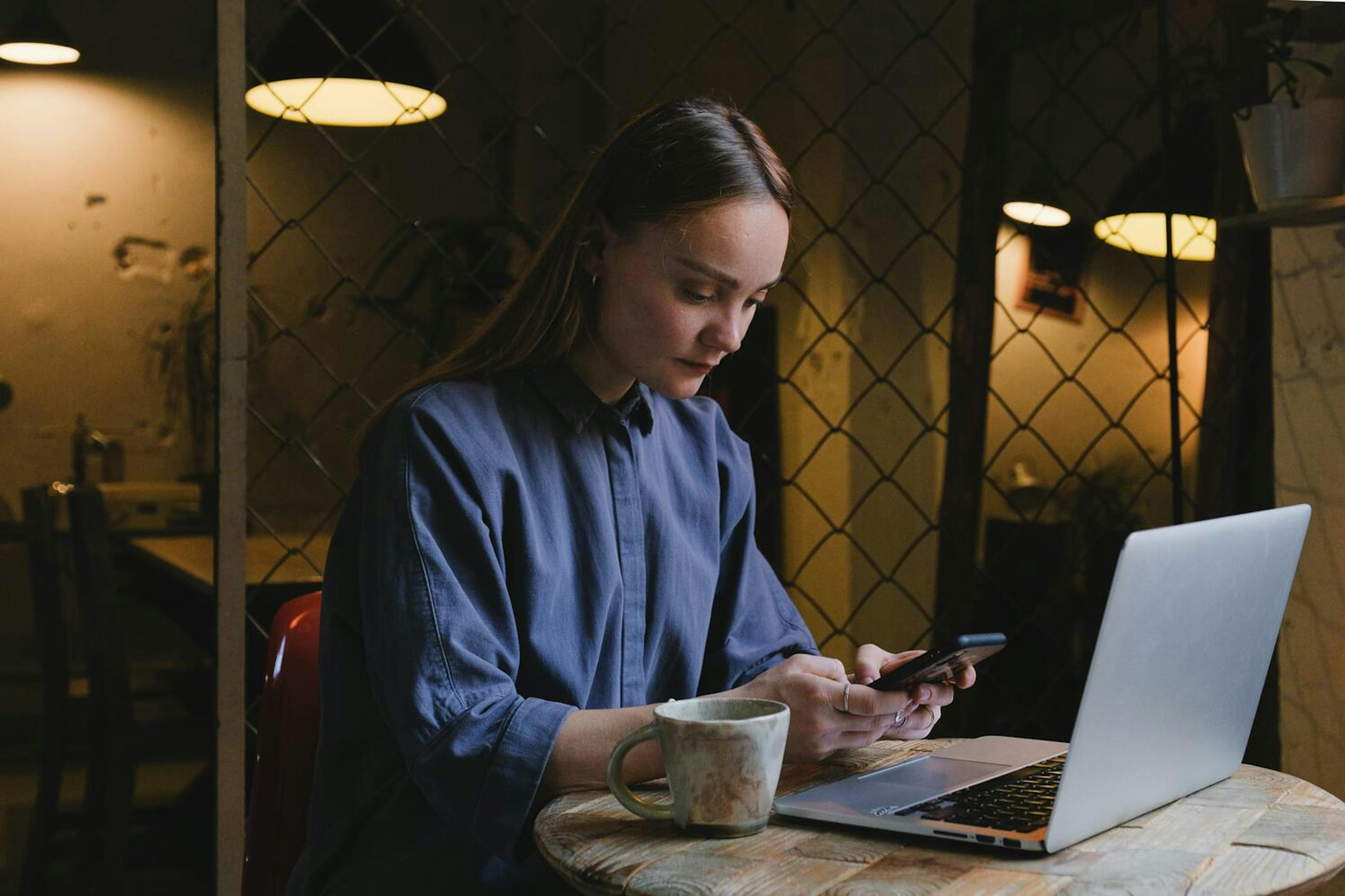 Image of a woman using her phone in front of a laptop