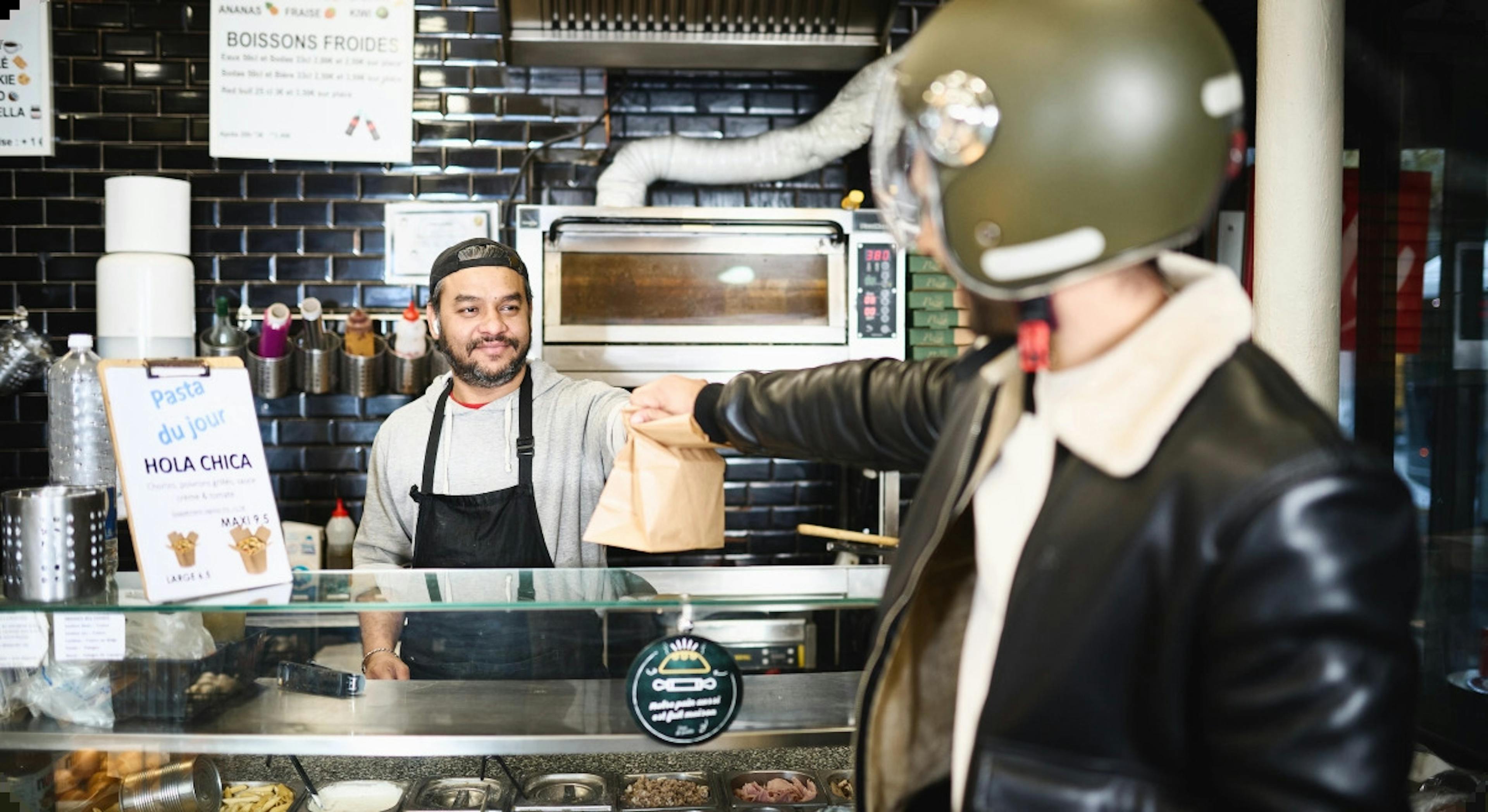 Image of a restaurant staff handing a food delivery package to the delivery rider