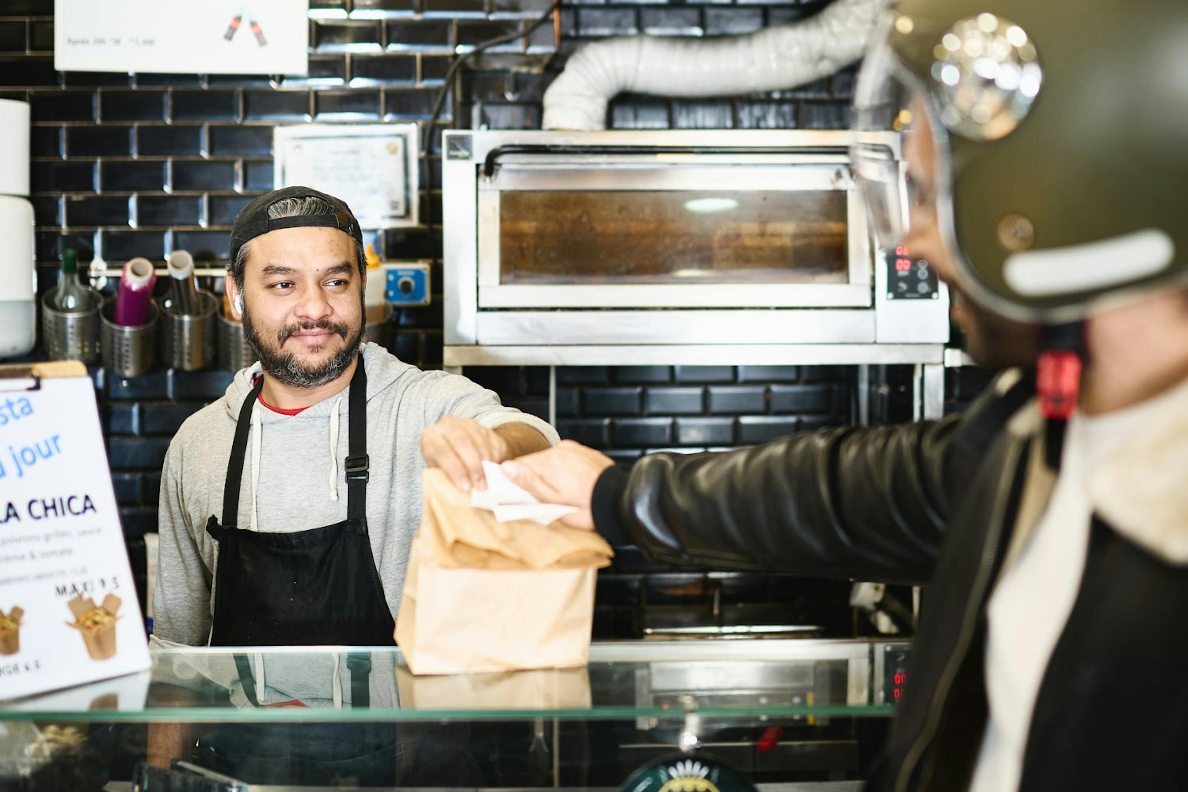 Image of a restaurant staff passing a food delivery package to a delivery courier