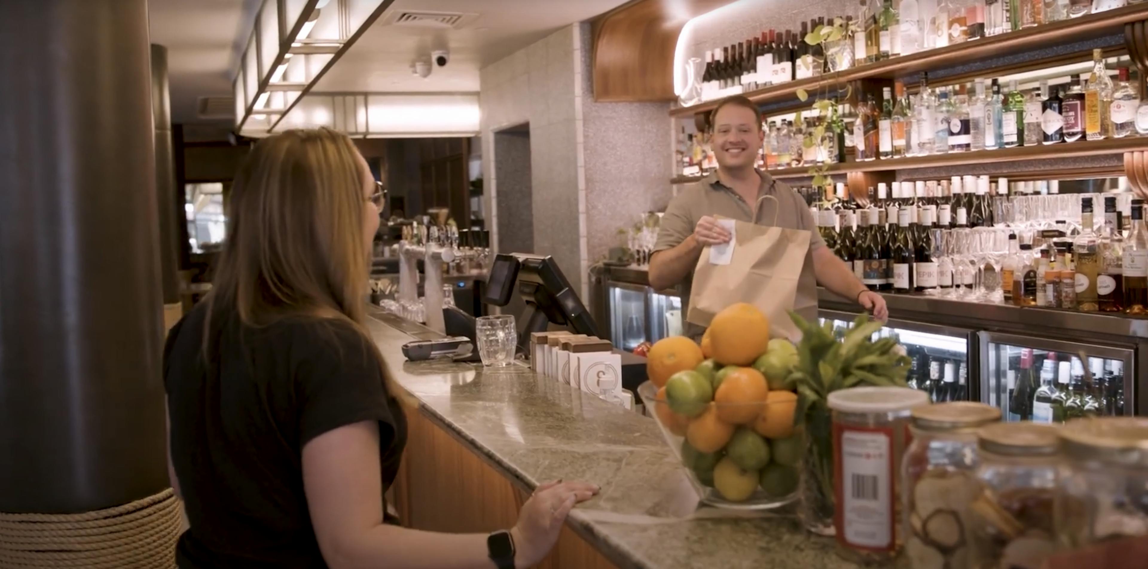 Image of a woman collecting a takeaway bag over the counter at Hotel Rose Bay