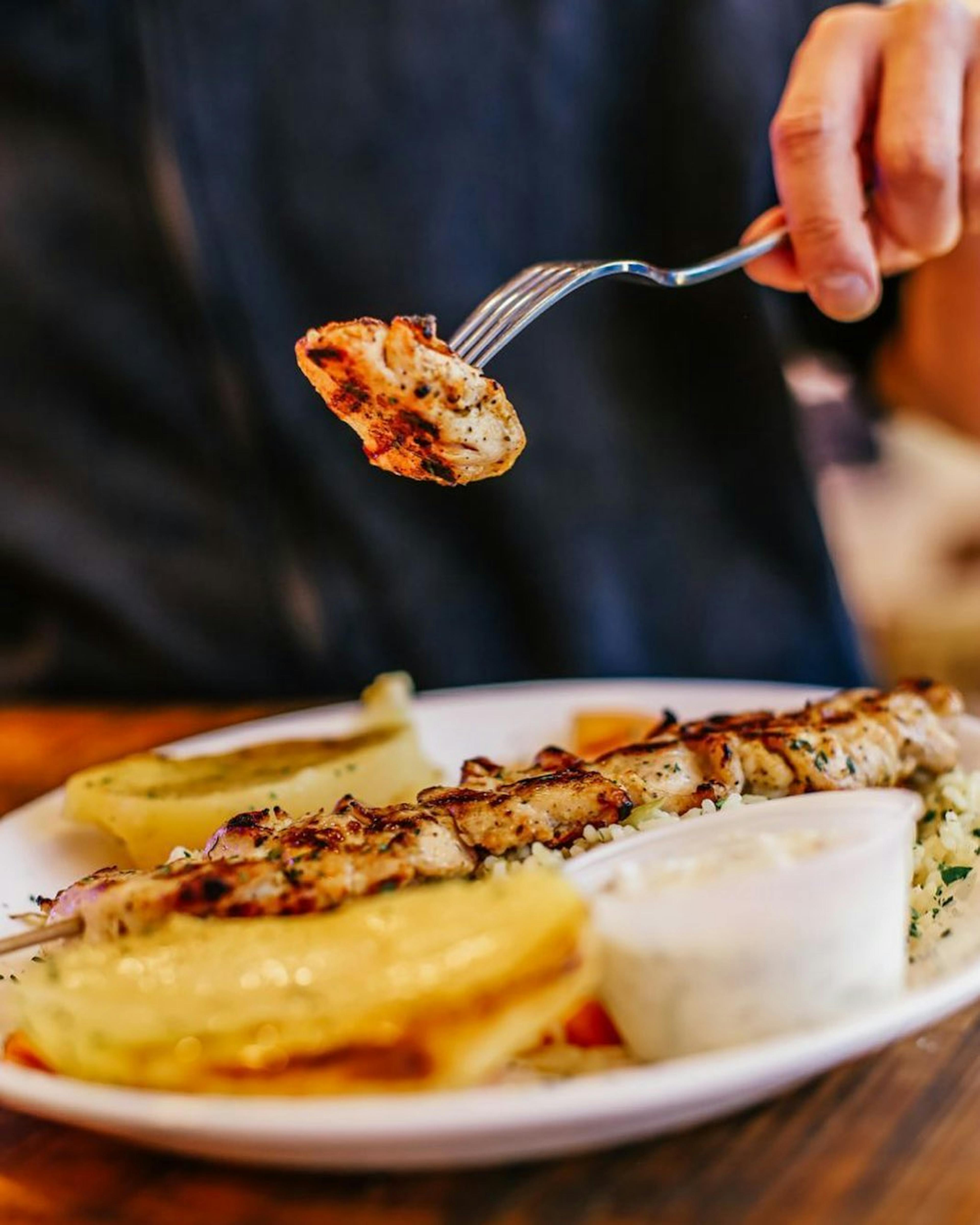 Image of someone putting a piece of meat from a Greek kabob onto their fork