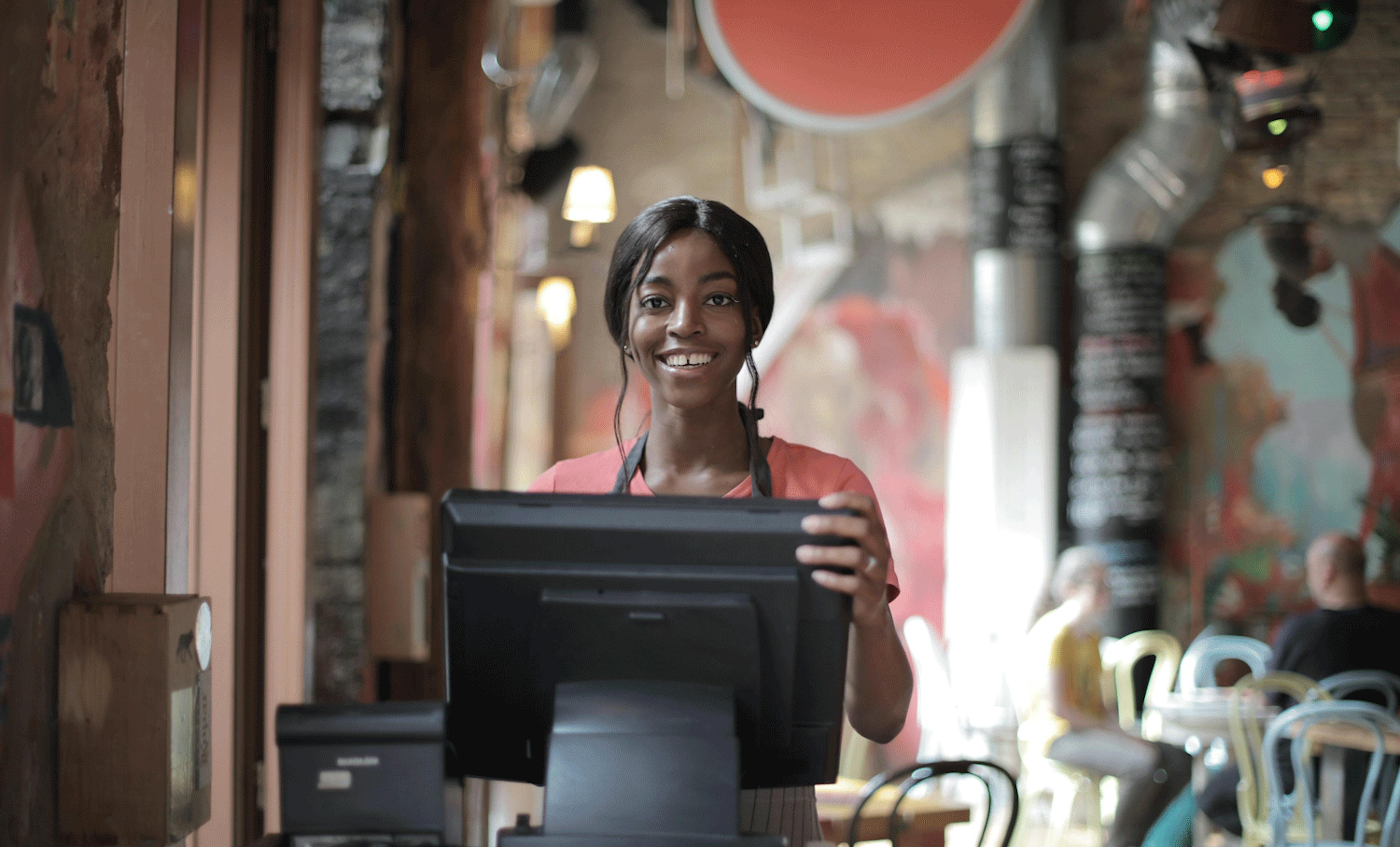 Image of a restaurant employee standing behind the POS system smiling