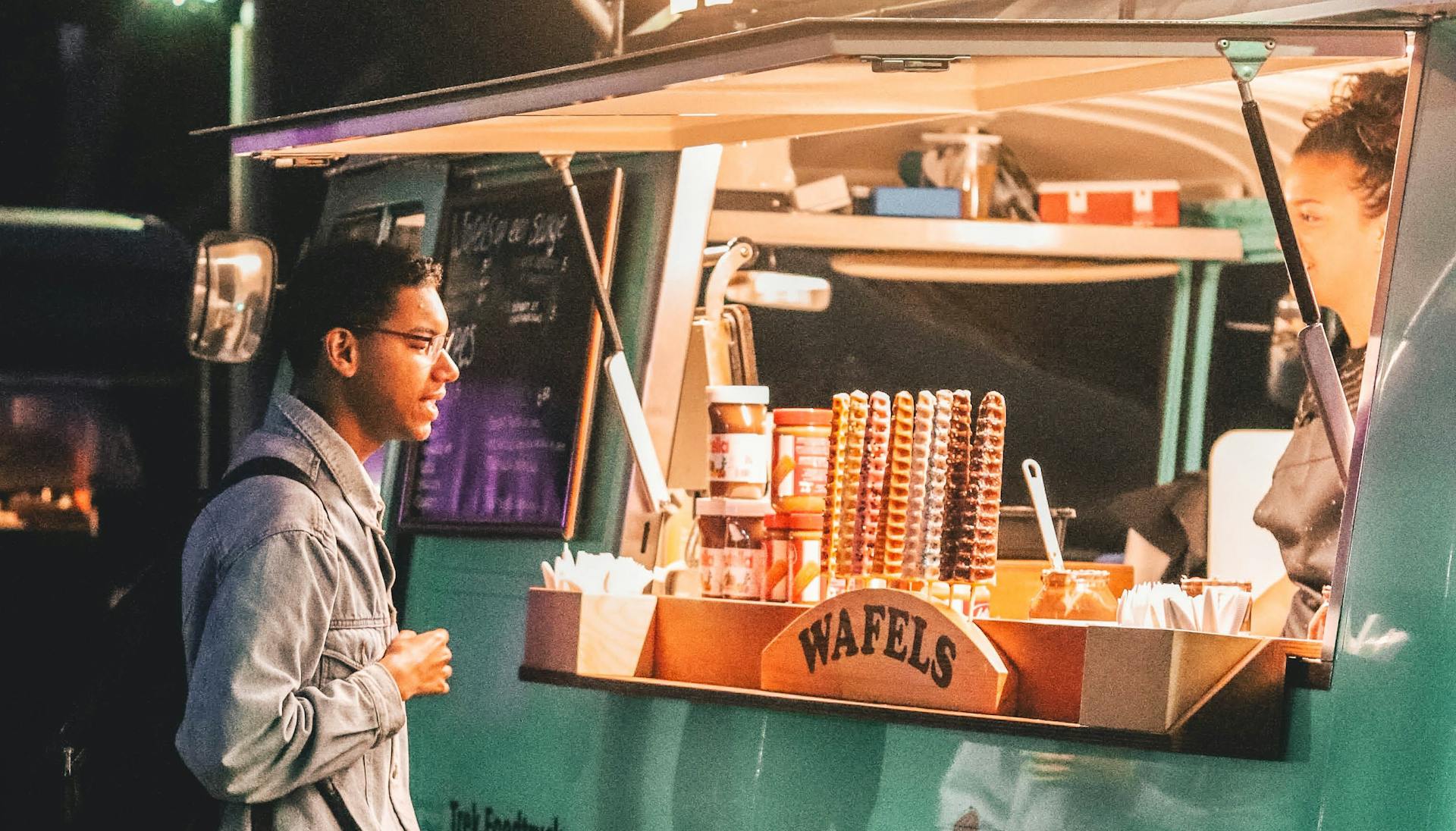 A delivery courier standing outside a food truck. 